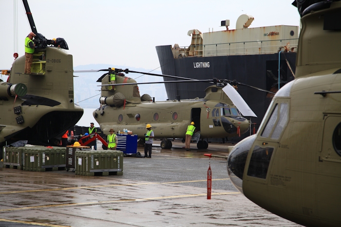 3 November 2013: On a cold and rainy November morning Boeing Maintenance crews work diligently to assemble the CH-47F Chinook helicopter fleet while the aircrews perform final airworthiness inspections prior to departing for Camp Humphreys, Republic of Korea. In the background sits the transport vessel "Lightning" in which the fleet and ground simulators arrived.