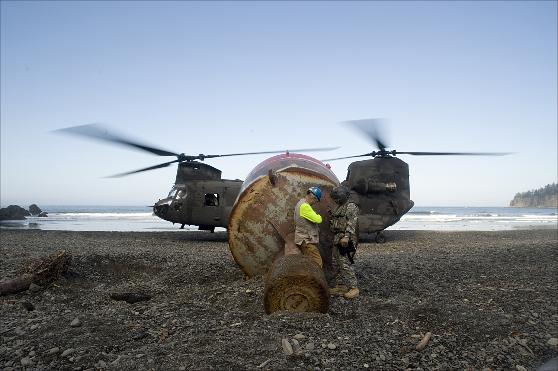 Shielding themselves from the wind and noise of the Chinook helicopter, Doug Cameron and a helicopter crewmen finish the rigging of the buoy.